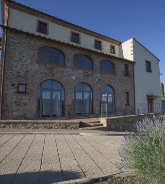 Casale in pietra con finestre ad arco e cespuglio di lavanda in primo piano.