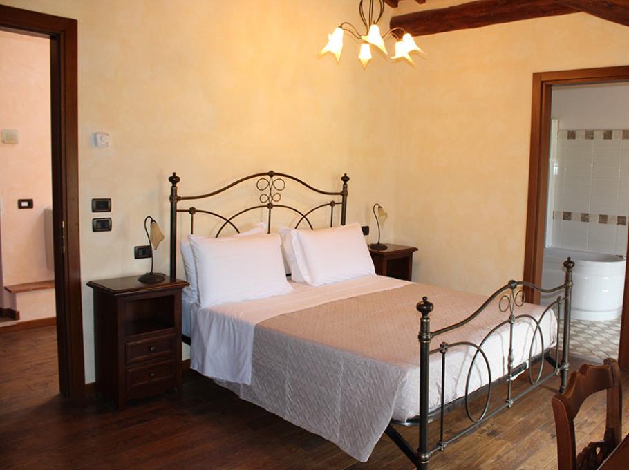 Camera accogliente con letto in ferro battuto, atmosfera calda e bagno elegante.