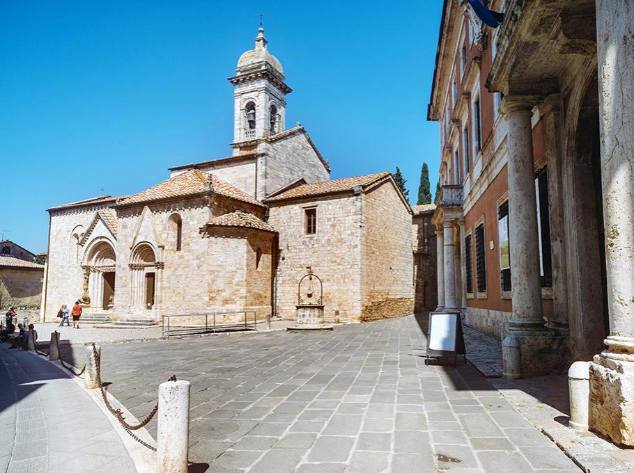 Chiesa medievale in pietra con campanile, situata in una piazza storica.